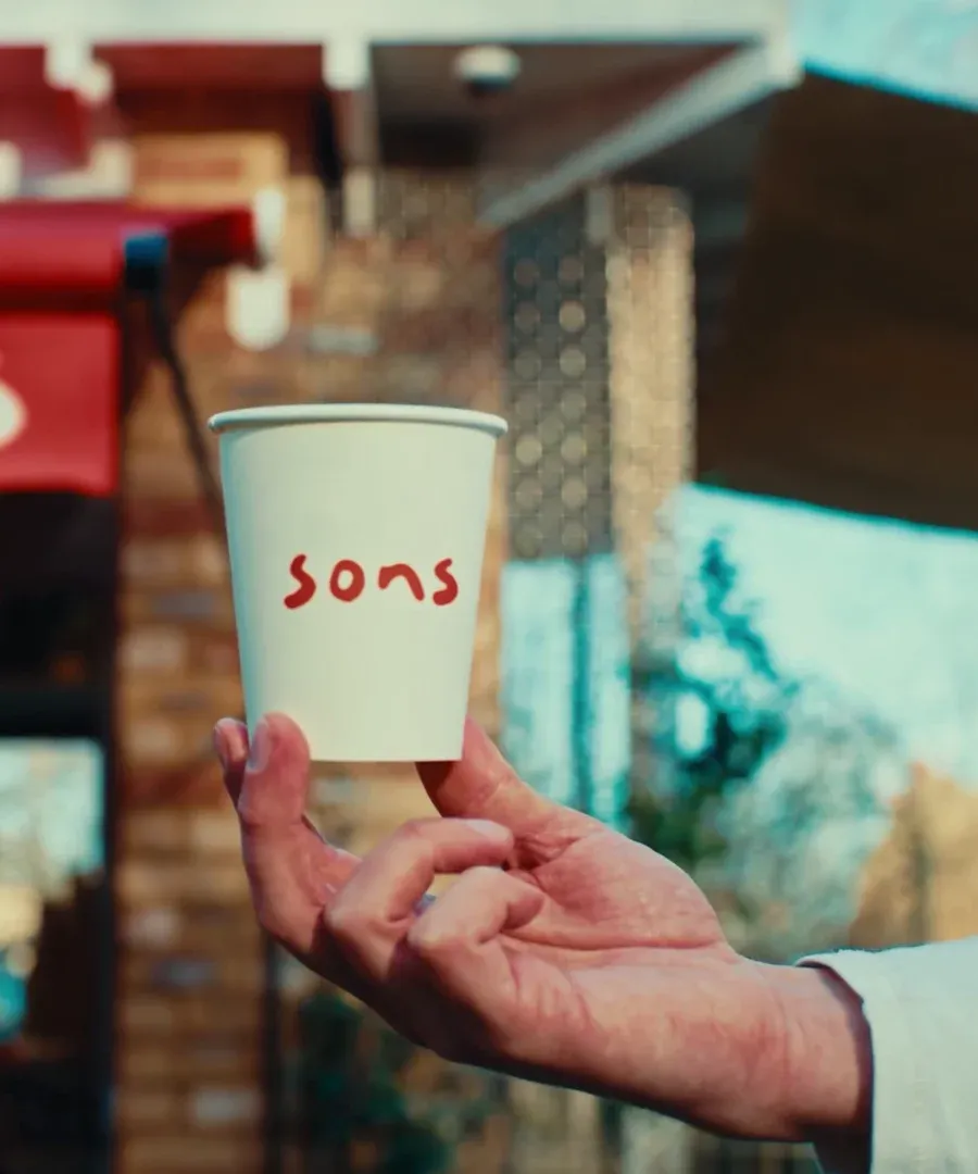 A sons takeaway cup held up in front of the kiosk